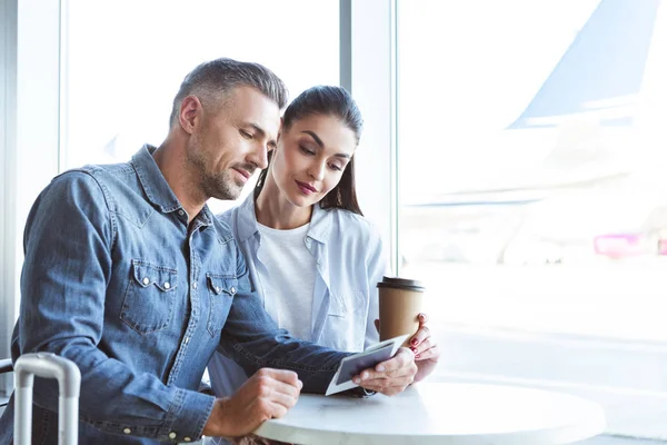 Couple sitting in the airport with coffee to go and looking at the tickets — Stock Photo