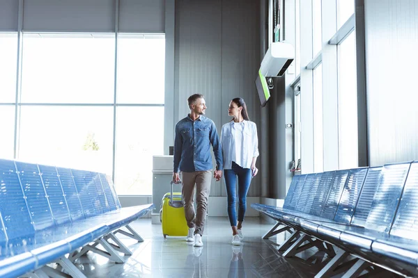 Homme et femme marchant avec un sac de voyage jaune à l'aéroport — Photo de stock