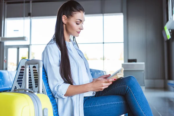 Hermosa mujer con equipaje amarillo leyendo un libro en el aeropuerto - foto de stock