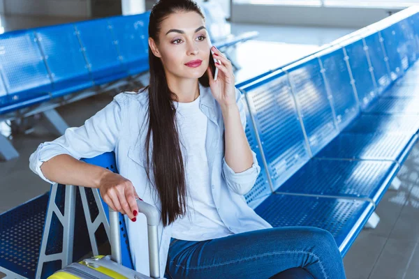 Beautiful girl talking on smartphone and waiting for her plane in the airport — Stock Photo