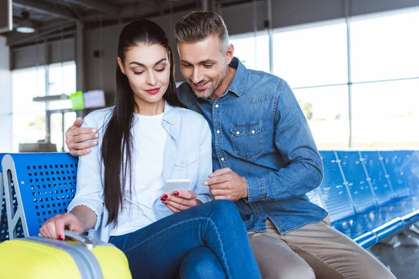 Uomo e donna seduti e utilizzando smartphone in aeroporto — Foto stock