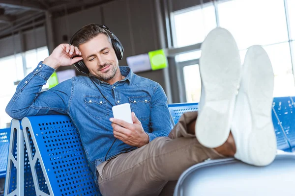 Uomo che sorride e ascolta la musica con cuffie e smartphone in aeroporto — Foto stock