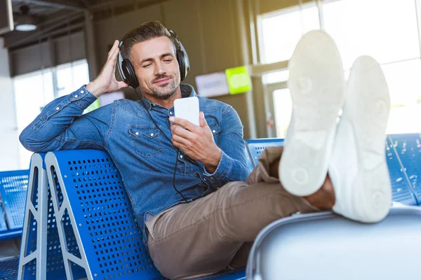 Mann hört Musik und checkt sein Handy am Flughafen — Stockfoto