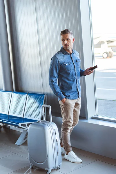 Hombre con una camisa azul manteniendo el teléfono en la mano y mirando algo en el aeropuerto - foto de stock