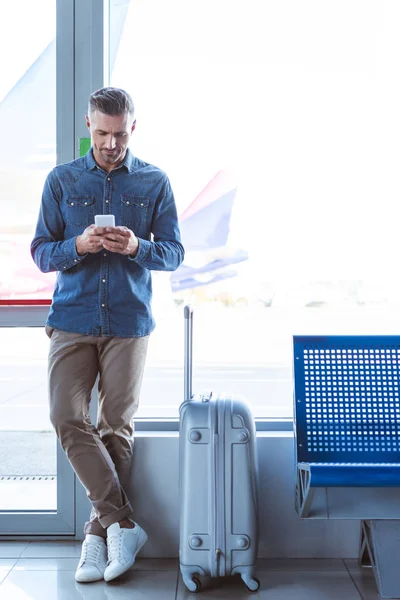 Elegante hombre de pie y mensajes de texto en el aeropuerto - foto de stock