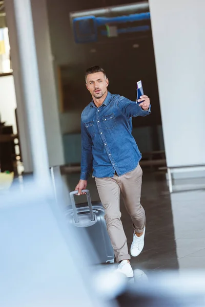 Hombre caminando en el aeropuerto y señalando algo con el pasaporte en la mano - foto de stock
