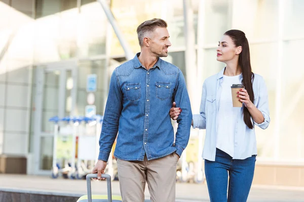 Feliz pareja de turistas cruzando peatonal, tomados de la mano y tirando de su equipaje - foto de stock