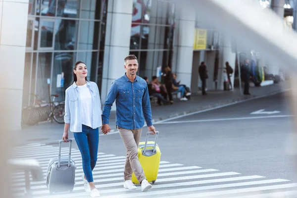 Пара туристов, переходящих пешеходов, держащихся за руки и тащащих свой багаж — стоковое фото