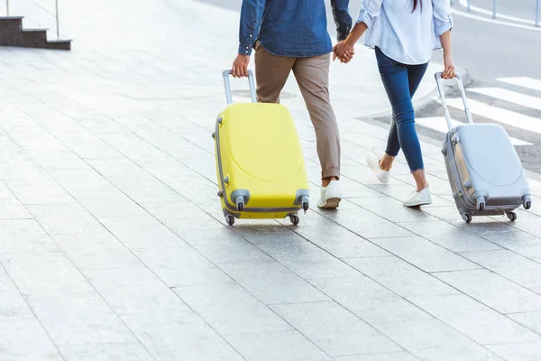 Обрізаний вид пари туристів, які тримають руки і тягнуть свій багаж — стокове фото