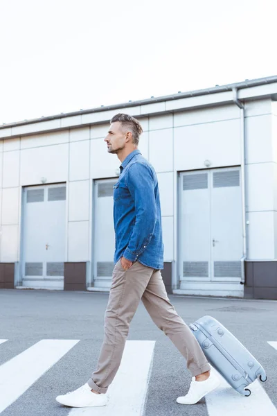 Side view of handsome adult man crossing pedestrian and pulling his luggage — Stock Photo