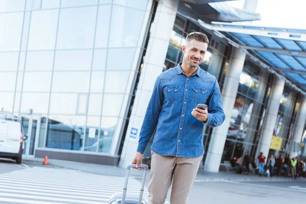 Bello uomo adulto che tiene smartphone e sorride alla fotocamera — Foto stock