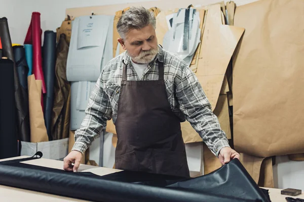 Mature tailor in apron working with leather at workshop — Stock Photo