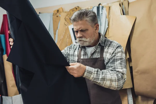 Concentrated handbag craftsman looking at leather in workshop — Stock Photo