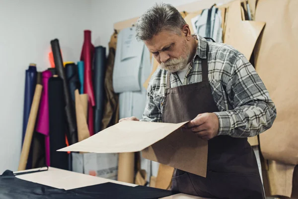 Reifer Handtaschenhandwerker in Schürze schaut sich in Werkstatt Pappe an — Stockfoto