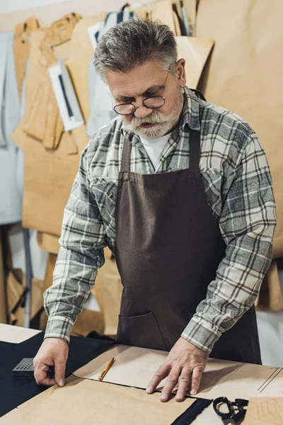 Middle aged male leather handbag craftsman in apron and eyeglasses working at studio — Stock Photo