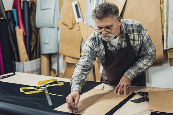 Serious mature male leather handbag craftsman in apron and eyeglasses working at studio — Stock Photo