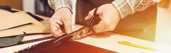 Cropped image of male handbag craftsman cutting leather by scissors at workshop — Stock Photo