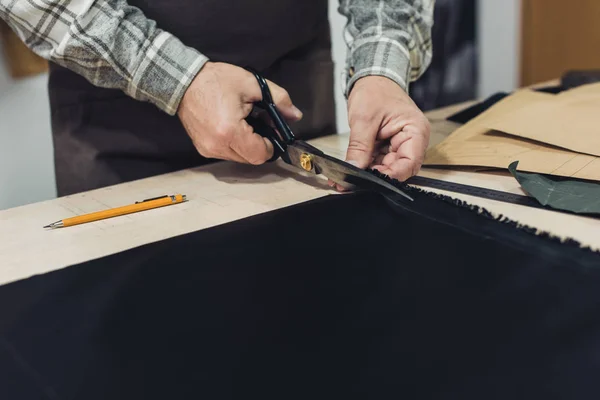 Cropped image of male handbag craftsman cutting leather by scissors at workshop — Stock Photo