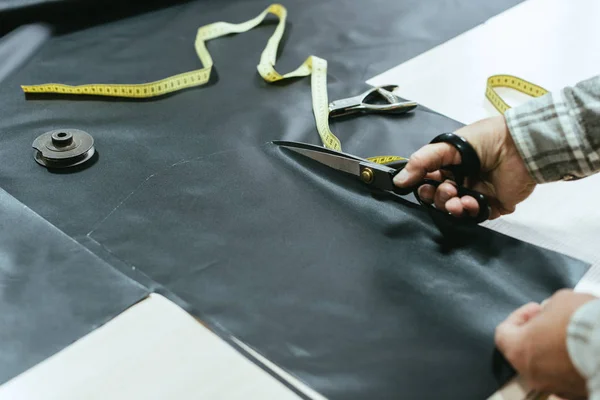 Cropped image of male handbag craftsman cutting leather by scissors at workshop — Stock Photo