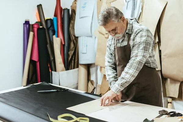 Middle aged tailor in apron making measurements at workshop — Stock Photo