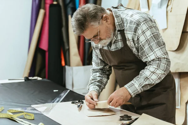 Male handbag craftsman in apron and eyeglasses working at studio — Stock Photo