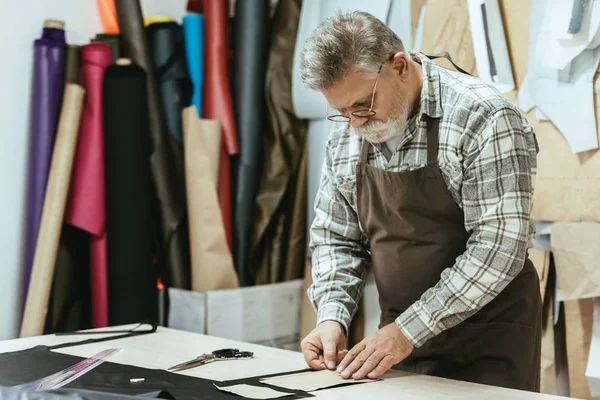 Hombre de mediana edad bolso artesano en delantal y gafas que trabajan en el estudio - foto de stock