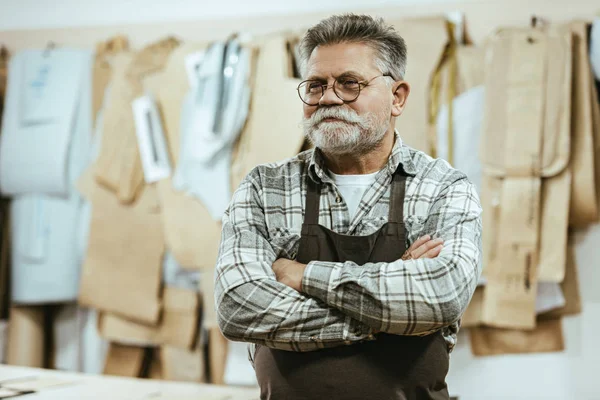 Glücklicher Handwerker mittleren Alters in Schürze und Brille steht mit verschränkten Armen im Atelier — Stockfoto