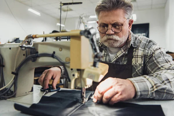 Male tailor in apron and eyeglasses working on sewing machine at studio — Stock Photo