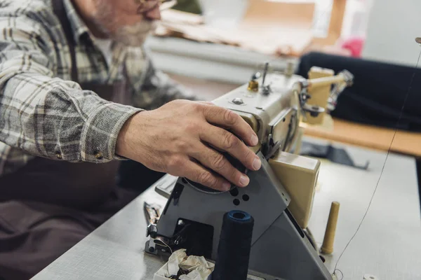 Teilansicht eines männlichen Schneiders in Schürze und Brille bei der Arbeit an der Nähmaschine im Atelier — Stockfoto