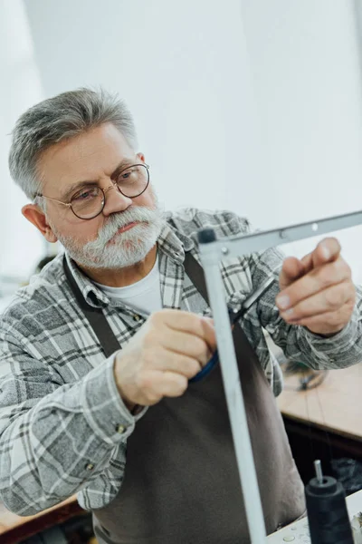 Портной среднего возраста в фартуке резки струны на швейной машине в мастерской — стоковое фото