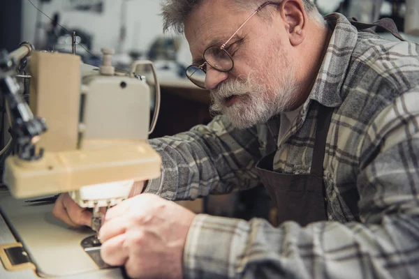 Hombre concentrado bolso artesano que trabaja en la máquina de coser en el estudio - foto de stock