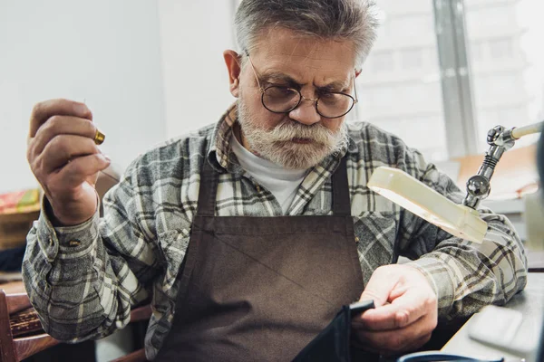 Männlicher Schneider mittleren Alters mit Brille und Schürze näht in der Werkstatt — Stockfoto