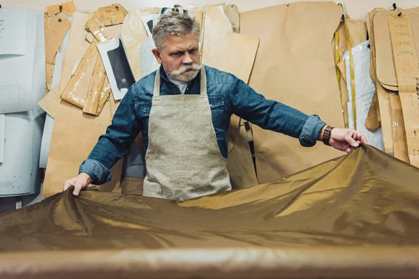 Selective focus of middle aged male handbag craftsman putting fabric on working table at studio — Stock Photo