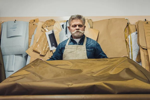 Confident middle aged male handbag craftsman putting fabric on working table at studio — Stock Photo