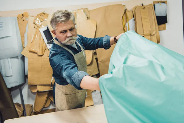 Maturo artigiano borsa maschile mettendo tessuto sul tavolo di lavoro in studio — Foto stock