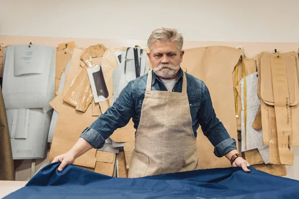 Hombre de mediana edad bolso artesano poner tela en la mesa de trabajo en el estudio - foto de stock