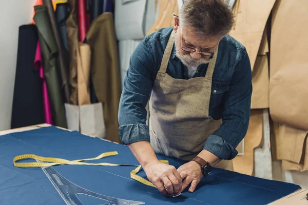 Male middle aged craftsman in apron making measurements on fabric at workshop — Stock Photo