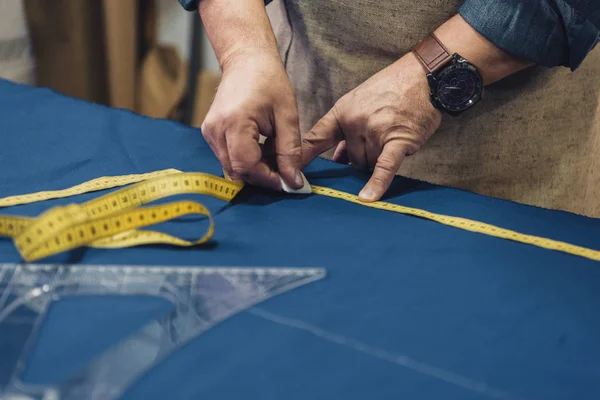 Cropped image of male craftsman in apron making measurements on fabric at workshop — Stock Photo