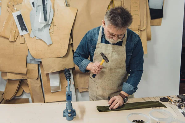 Männlicher Handtaschenhandwerker mittleren Alters arbeitet im Atelier mit Hammer — Stockfoto