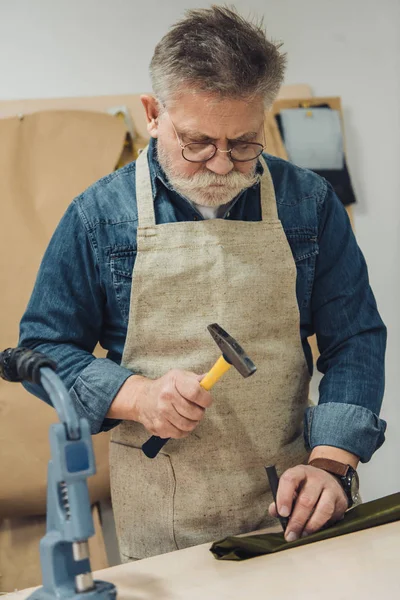 Serious middle aged male handbag craftsman working with hammer at studio — Stock Photo