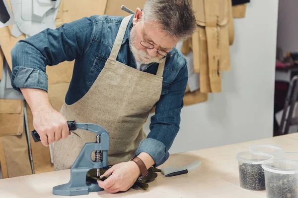 Hombre maduro concentrado bolso artesano que trabaja con herramienta en el estudio - foto de stock