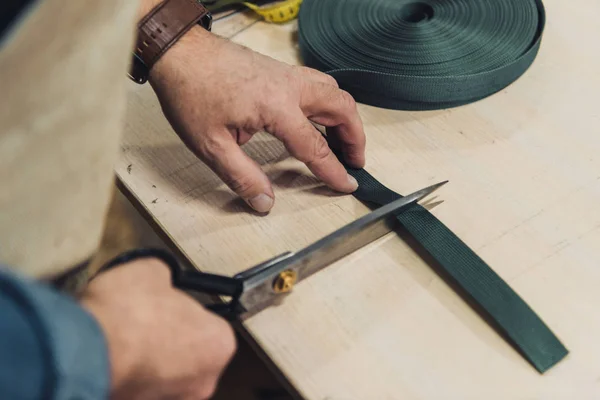 Abgeschnittenes Bild eines männlichen Handtaschenhandwerkers, der in der Werkstatt mit der Schere Stoff schneidet — Stockfoto