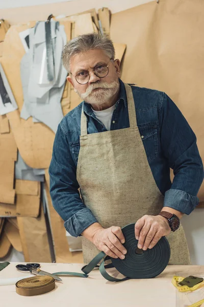 Seriöser Handwerker mittleren Alters mit Brille und Schürze, der bei der Arbeit im Atelier in die Kamera schaut — Stockfoto