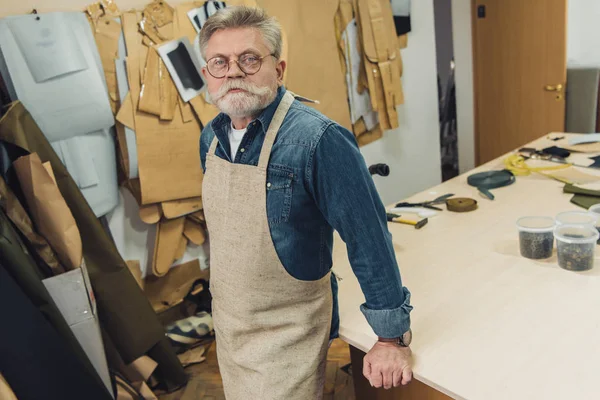 Ernster Handwerker mittleren Alters in Schürze blickt in die Kamera im Atelier — Stockfoto