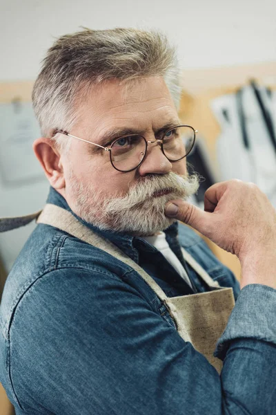 Pensive middle aged male craftsman in apron posing at workshop — Stock Photo