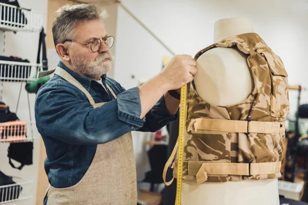 Concentrated middle aged male tailor making measurements on military vest at workshop — Stock Photo