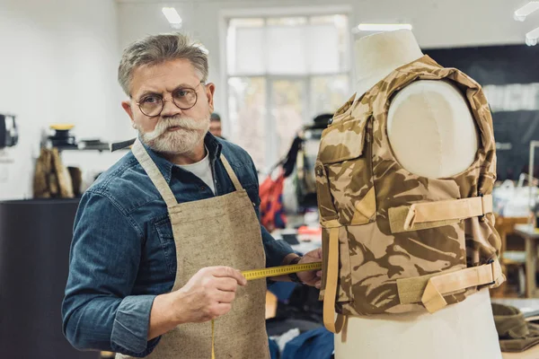 Selbstbewusster Mann mittleren Alters maßschneidert in Werkstatt an Militärweste — Stockfoto