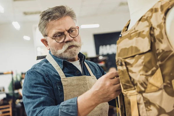 Centrado de mediana edad sastre masculino haciendo mediciones en chaleco militar en el taller - foto de stock