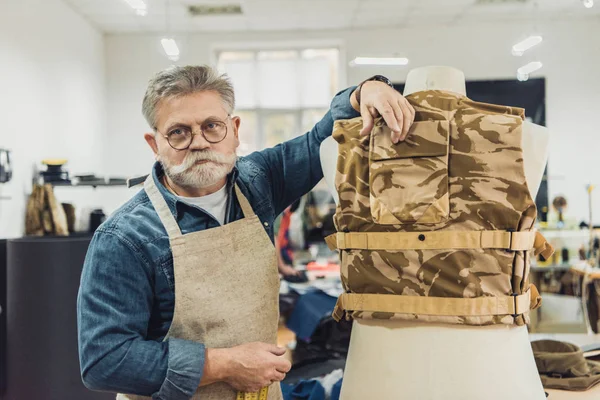 Cheerful middle aged male tailor standing near military vest at studio — Stock Photo