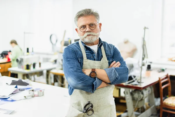 Serious mature male craftsman in apron posing with crossed arms at workshop — Stock Photo